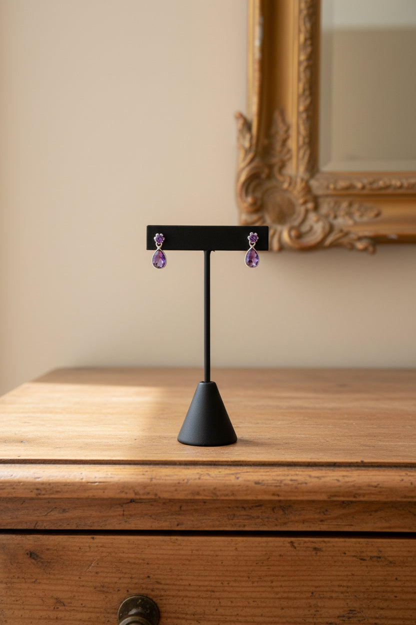 Amethyst drop earrings displayed on a stand, featuring large amethyst gemstone dangling from smaller amethyst gemstones, set in a sterling silver mounting.