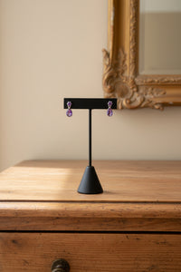 Thumbnail for Amethyst drop earrings displayed on a stand, featuring large amethyst gemstone dangling from smaller amethyst gemstones, set in a sterling silver mounting.