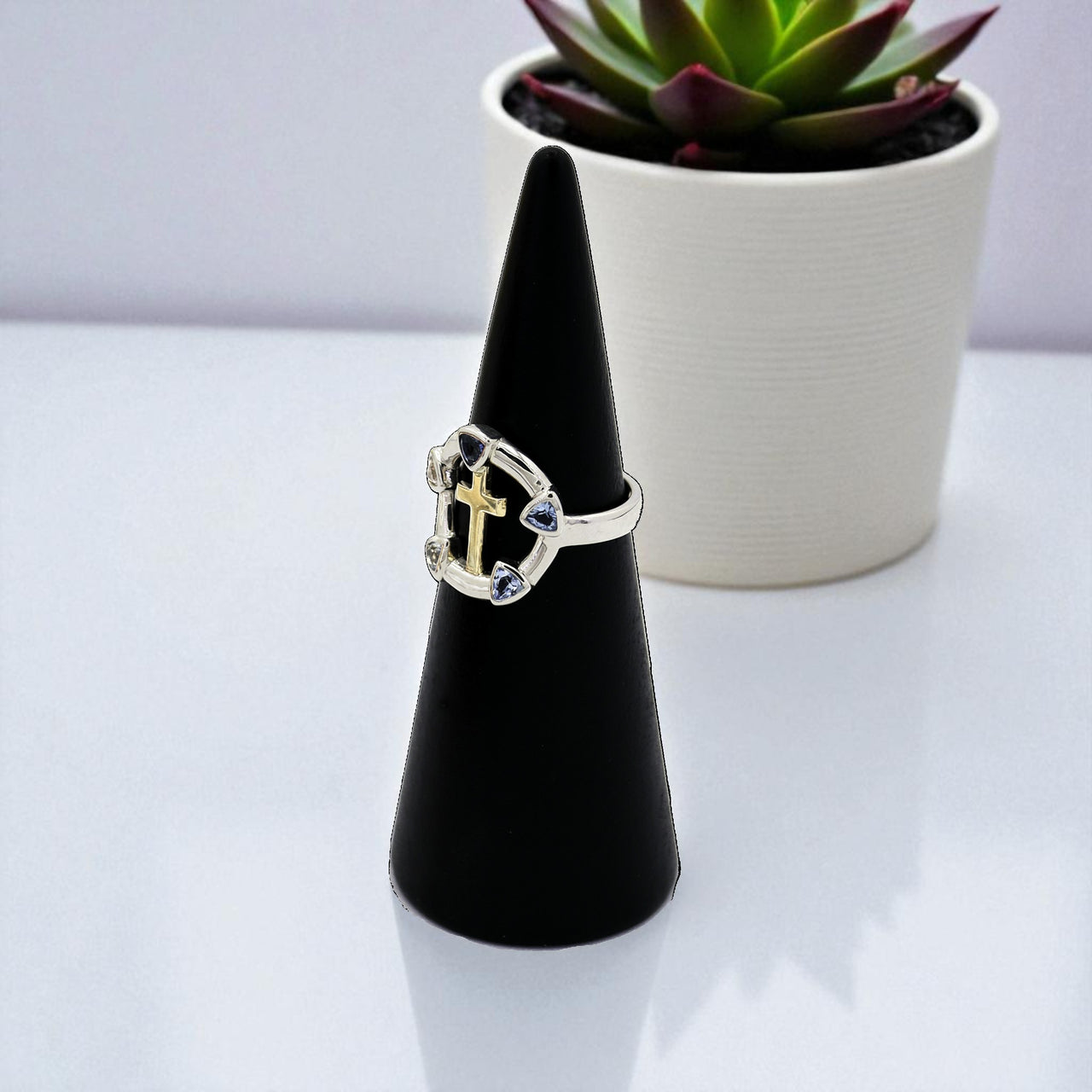 Silver ring on a black cone-shaped stand with a potted plant in the background
