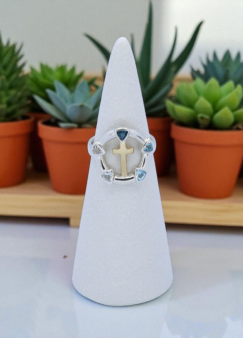 Ring with a cross design on a white cone stand with plants in the background