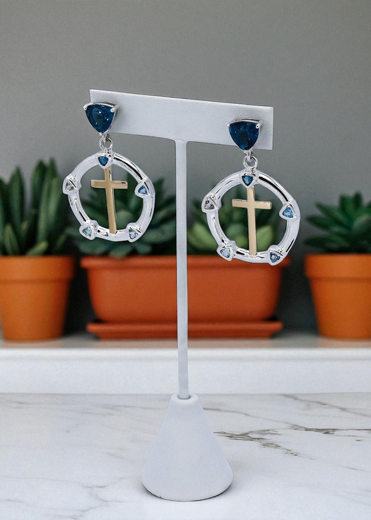 Earrings with crosses on a white stand with plants in the background
